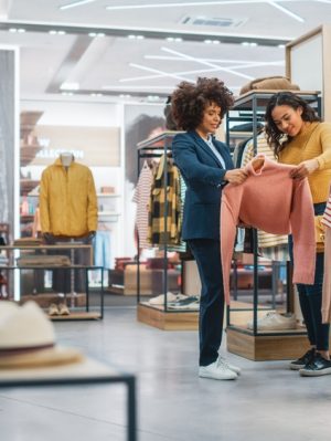 Customers Shopping In Modern Clothing Store Retail Sales Associate Assists